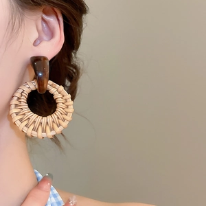 Macro detail of round woven rattan drop earrings featuring a smooth dark brown connector piece