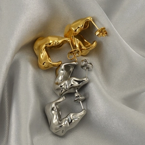 Detailansicht goldener und silberner unregelmäßiger Ohrringe auf grauem Seidenhintergrund