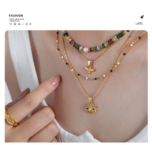Detailed view of layered gold-plated bird and evil eye charms on a beaded necklace set