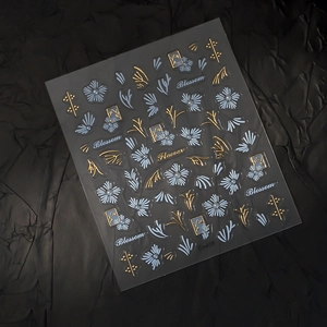 Macro shot of 3D floral nail stickers with gold outlines and pearl accents on black paper
