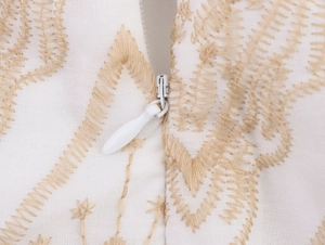 Detailed close-up of golden wavy embroidery and white invisible zipper on dress fabric