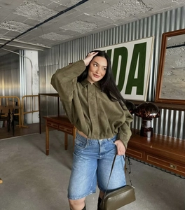 Dettaglio giacca bomber in camoscio verde oliva abbinata a pantaloncini di jeans