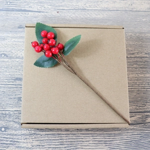 Artificial red berry stems with green leaves on wooden background for DIY craft decoration