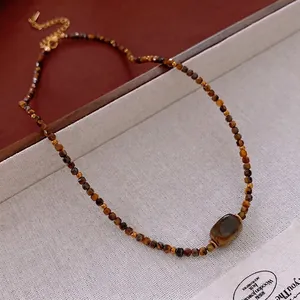 Tiger eye beaded necklace with oval gemstone and gold lobster clasp on textured surface
