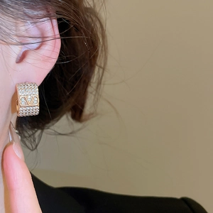 Close-up of gold-plated V-logo earrings with cubic zirconia worn by a model