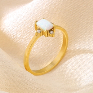 Close-up of gold titanium ring with rectangular white opal and zircon on silk fabric