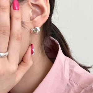 Close-up of a high-polish silver heart stud earring worn by a model in a pink shirt