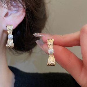 Dettagli di orecchini a fiocco dorato pieghettato con inserto di perle e perni in argento