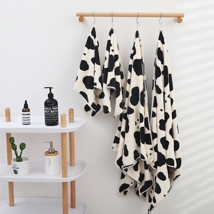 Soft coral fleece towel set with cow print hanging on a wooden rack in a modern bathroom
