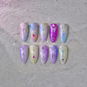 Détail d'ongles dégradés lilas et bleus avec papillons blancs et strass scintillants