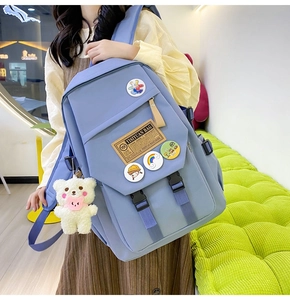Detail of light blue nylon student backpack featuring decorative badges and a plush bear pendant