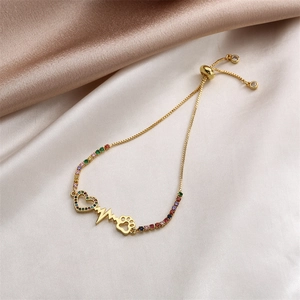 Detail of adjustable gold bracelet with colorful zircon heart, heartbeat, and paw charms