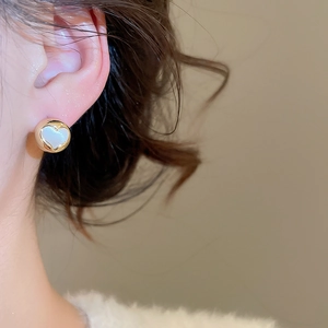 Close-up of heart-shaped gold stud earring with white inlay on a model's ear