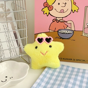 Close-up of yellow plush star pendant with pink heart sunglasses on a warm background