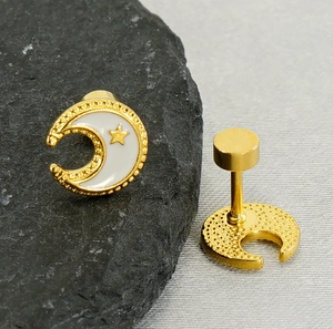 Detailed close-up of 18k gold moon and star stud earrings on a textured stone surface