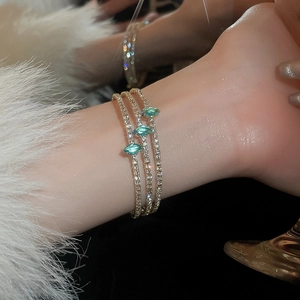 Detail of a three-layer gold bracelet with green marquise-cut stones on a model's wrist