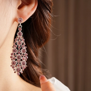 Vista detallada de pendientes plateados con circonitas rosas y diseño de calado elegante
