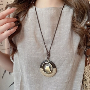 Detail of wooden leaf pendant necklace with metal bird and jute rope wrap on linen