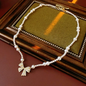 Detail of pearl necklace featuring a golden bow pendant with sparkling cubic zirconia