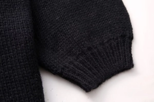 Detailed close-up of thick black knit fabric featuring ribbed cuffs on long sleeves