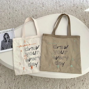 Detailed close-up of embroidered canvas tote bags with draw your every day artistic text