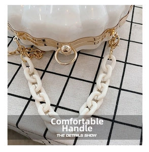 Detail of shell-shaped white textured bag with gold metal frame and acrylic chain