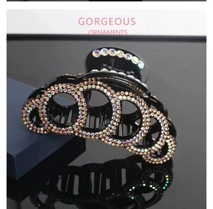 Macro detail of black claw clip with circular colorful rhinestone patterns on high-gloss finish