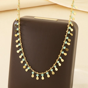 Detail of gold necklace with mint green beads and water drop pendants on box