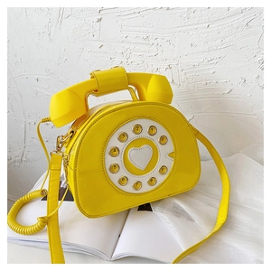 Close-up of a creative bright yellow telephone-shaped crossbody bag in shiny patent leather