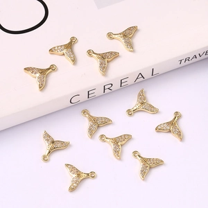 Detail shot of golden fish-tail pendants with cubic zirconia inlay on a white surface