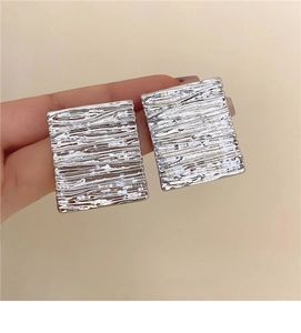 Detail showing hand holding silver rectangular earrings with irregular pleated texture