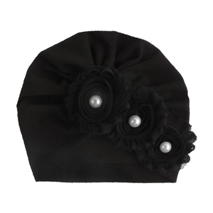 Schwarze Baby-Turban-Mütze mit drei Stoffblumen und weißen Perlen auf weißem Hintergrund