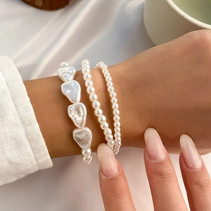 Close-up of stacked baroque and round faux pearl bracelets on wrist with white silk