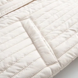 Close-up of cream quilted jacket featuring horizontal stitching and side pocket detail