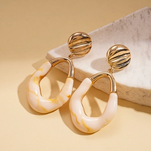 Detail of geometric resin earrings with gold metallic texture on minimalist stone display