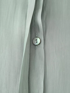 Macro view of light green fabric texture and natural shell button on a women's blouse