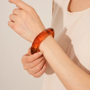 Detail of amber resin bangle showing natural texture on model's wrist in minimalist setting