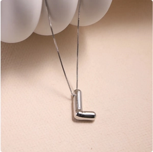 Macro shot of silver metal balloon style letter L pendant on fine box chain necklace