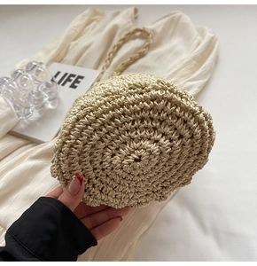 Detail shot of the woven texture and handle of a beige straw bucket bag on white fabric