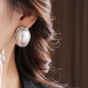 Close-up of a large oval pearl earring with silver polished frame on a model ear
