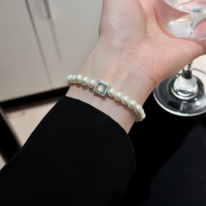 Detail of elegant pearl bracelet with blue gemstone square pendant on female wrist