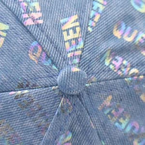 Vista macro della scritta QUEEN olografica sul tessuto denim blu del cappello baseball