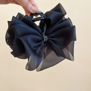 Dettaglio del fermaglio a fiocco in organza nera con strass scintillanti e strati