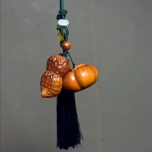 Detailed wood carving of a peanut and pumpkin pendant with long black silk tassel