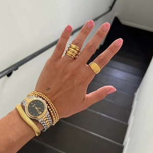 Detail view of layered 18K gold-plated beaded bracelets and textured wide rings