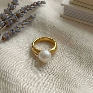 Artistic close-up of 18k gold plated titanium ring with a large white pearl on fabric
