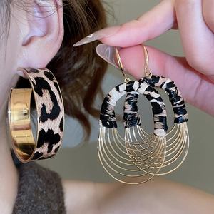 Detail of leopard print oval pendant earrings and C-shaped hoops with gold metal finish