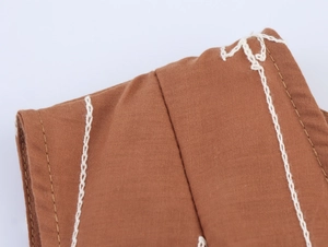 Détail de la texture du lin marron avec surpiqûres blanches contrastées et broderie