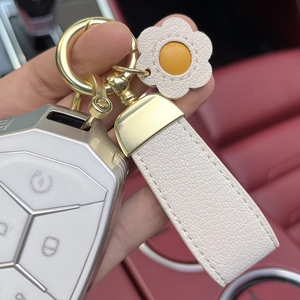 Detail of cream leather daisy keychain with a champagne gold car key shell on red interior