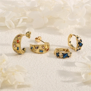 Close-up of gold earrings with blue and multi-color zircons on a white textured background